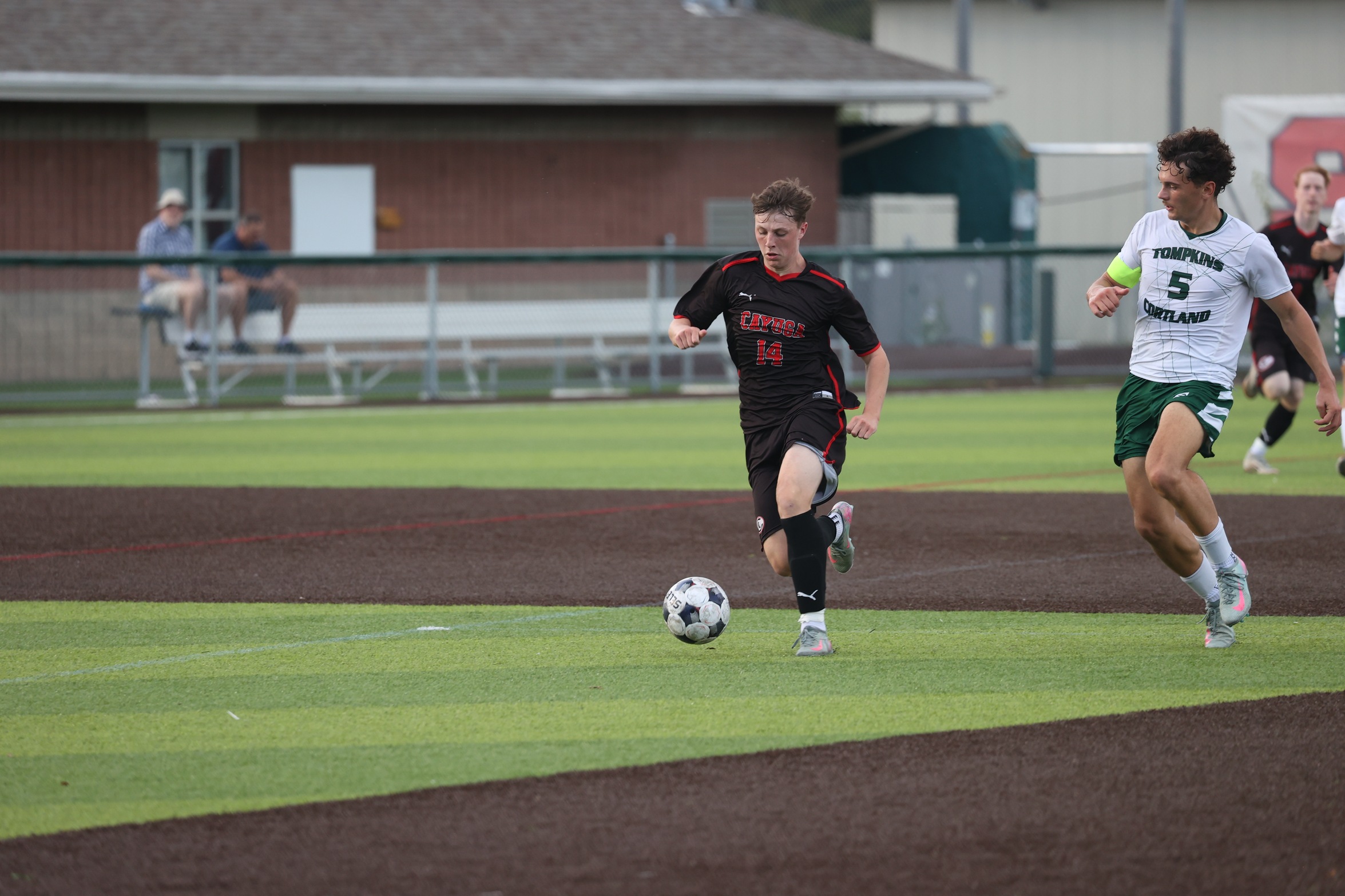 A Cayuga player dribbles the ball while a Tompkins Cortland Community College defender runs next to him.